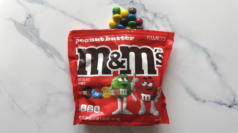 Bag of peanut butter M&M's and a few candies on marble surface