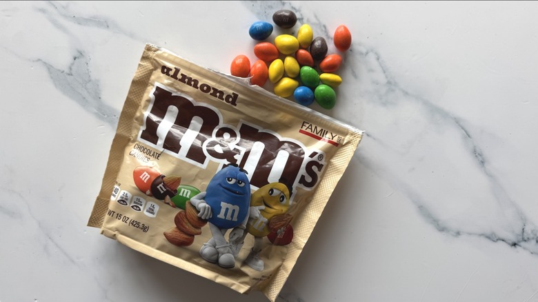 Bag of almond M&M's and a few candies on marble surface