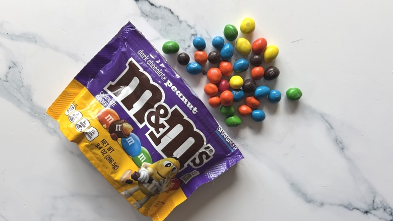 Bag of dark chocolate peanut M&M's and a few candies on marble surface