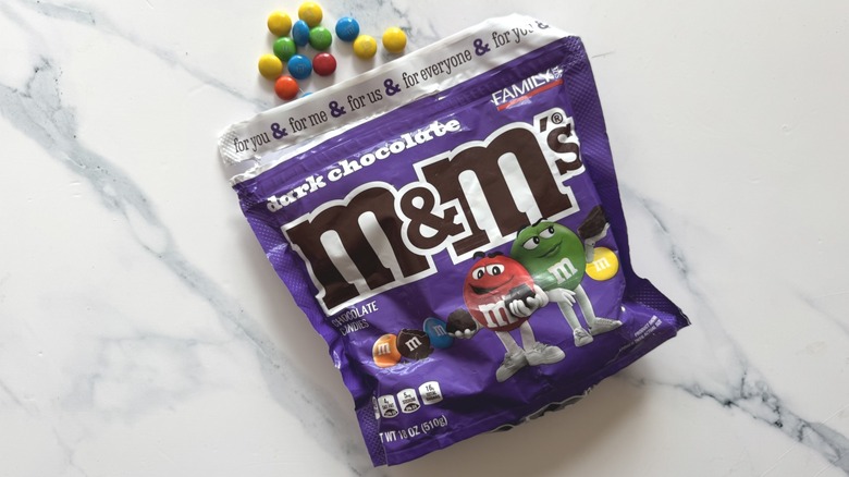 Bag of dark chocolate M&M's and a few candies on marble surface