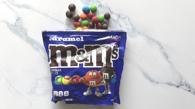 Bag of caramel M&M's and a few candies on marble surface