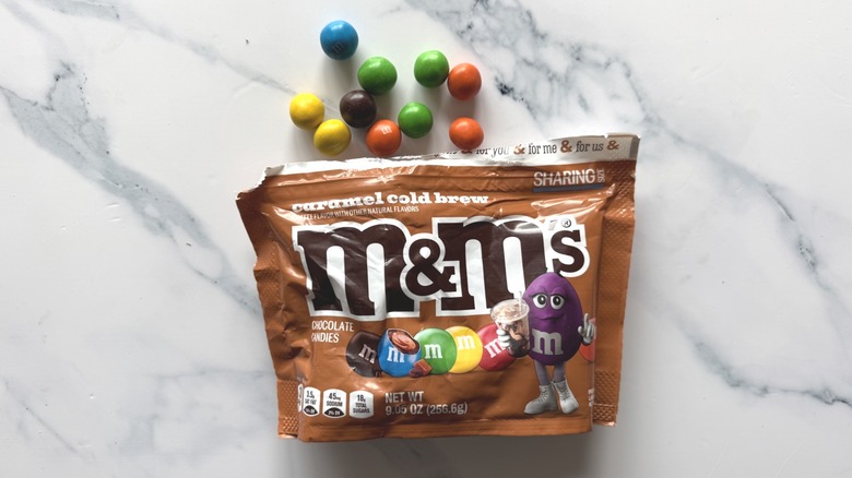 Bag of caramel cold brew M&M's and a few candies on marble surface