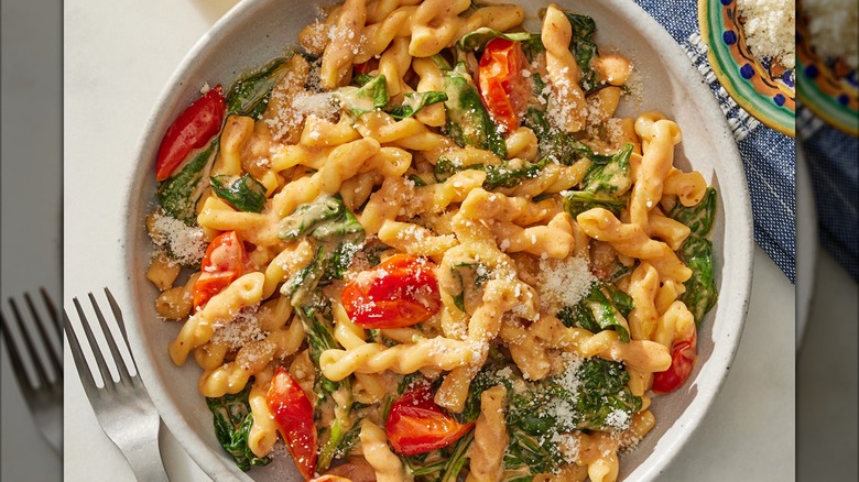 A white bowl of pasta with greens, tomatoes, and creamy sauce