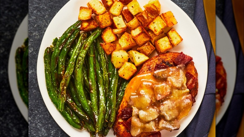 A dish of green beans, potatoes, and smothered chicken on a white plate