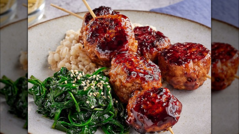 A plate with barbecued meatballs, barely, and cooked spinach