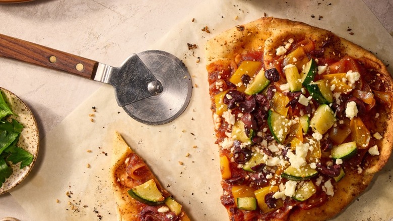 A flatbread pizza with a pizza roller on parchment paper
