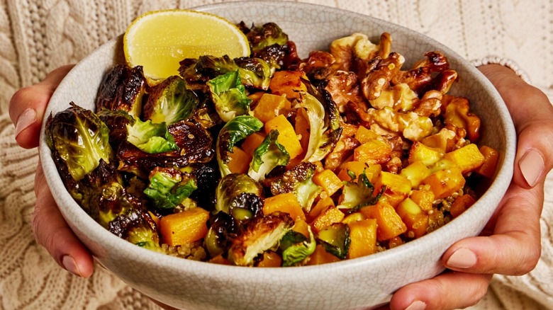 A woman holding a bowl of roasted brussel sprouts and other vegetables