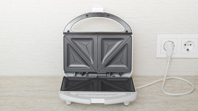 A sandwich maker that's open and plugged into a wall outlet
