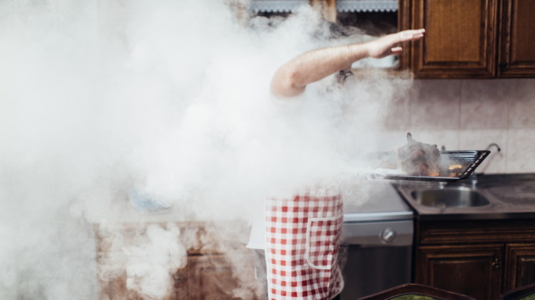 Person in a red and white checked apron removing burnt, smoking chicken from an oven