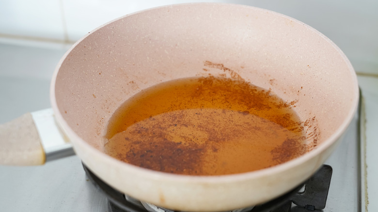 Leftover oil in a white frying pan on a cold stove