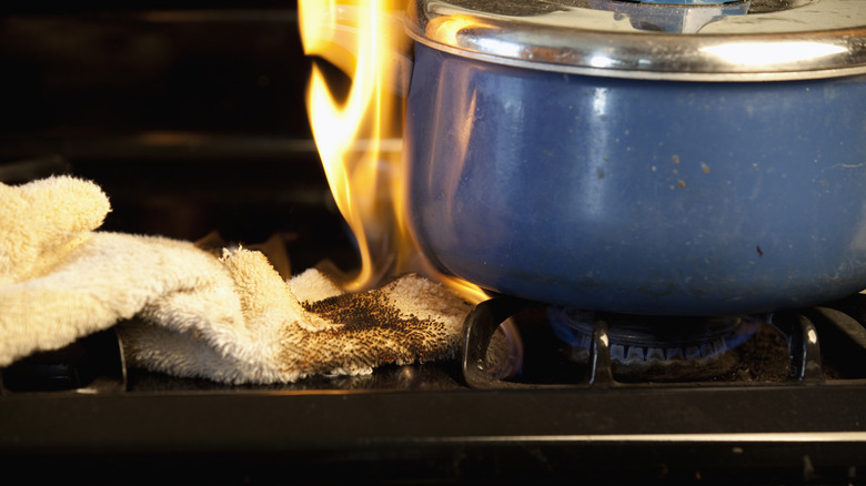 A kitchen towel on fire on a stove burner next to a blue pot