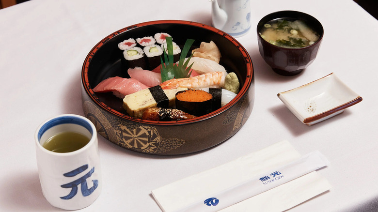 A bowl of sushi alongside a mug of green tea and miso soup