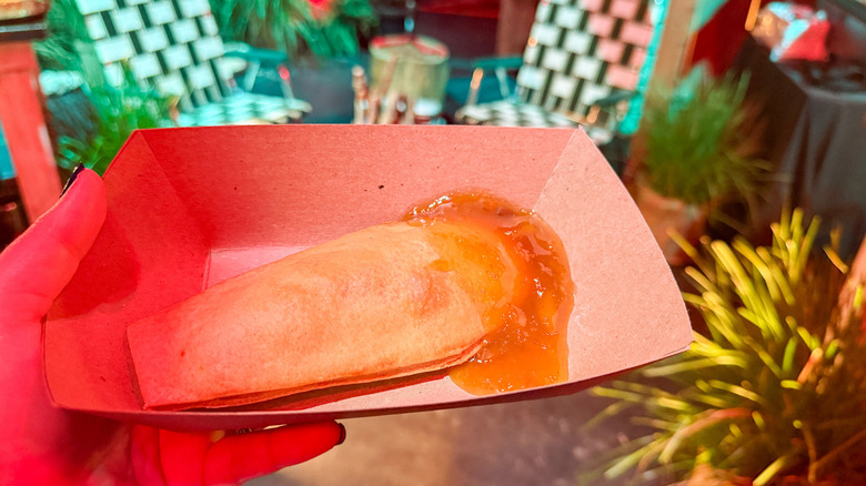 Hand holding a coffin-shaped pastry in a takeout box