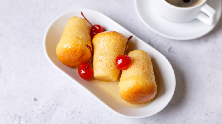 Three babas au rhum on a white oval plate garnished with maraschino cherries