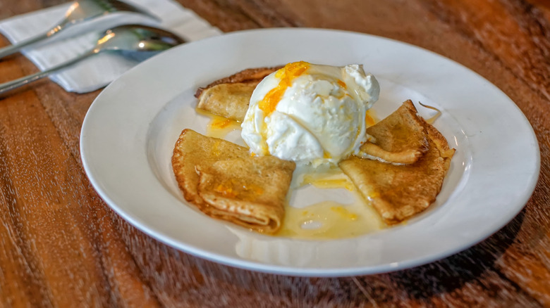 White plate of crèpes Suzette with vanilla ice cream and orange sauce