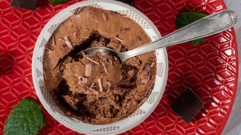 Close up of a bowl of mousse au chocolate on a red plate garnished with shaved chocolate