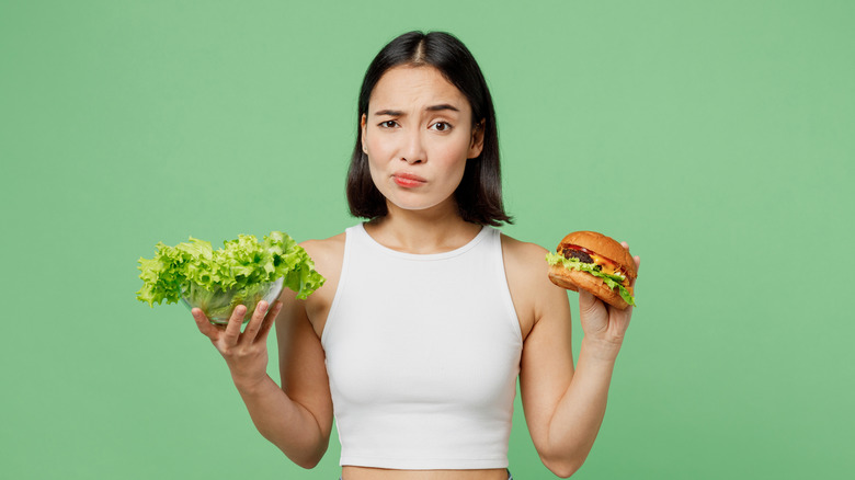 Woman frowning and holding lettuce and a hamburger