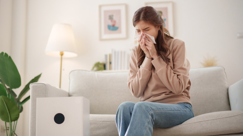 Woman sitting on couch with a tissue to her nose
