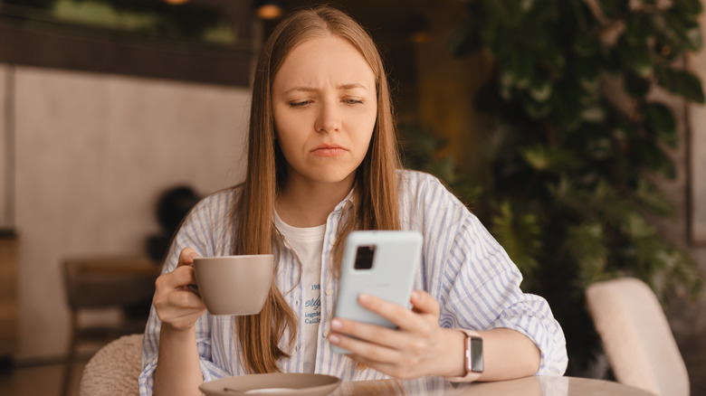 Woman holding coffee frowning at phone