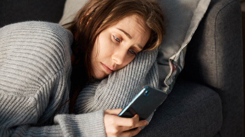 Tired or sick woman laying down looking at phone