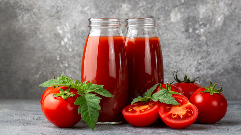 Two thick glass bottles of tomato juice surrounded by fresh tomatoes