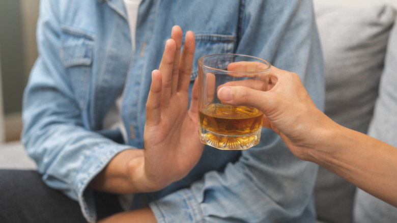 A person holding out a glass of alcohol and another person holding up a hand to refuse it