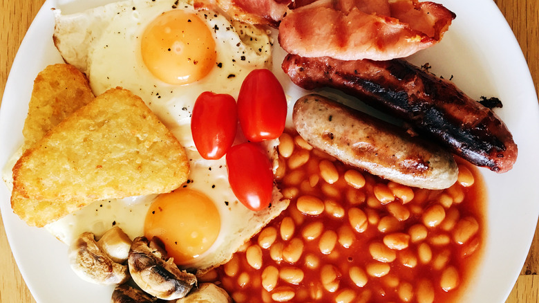 A full English breakfast, including links, fried eggs, bacon, and baked beans, on a white plate