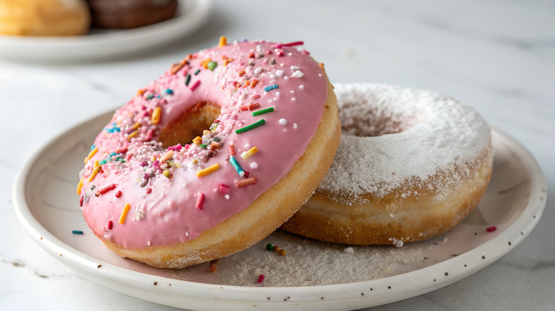 Two sprinkled and powdered donuts on a plate