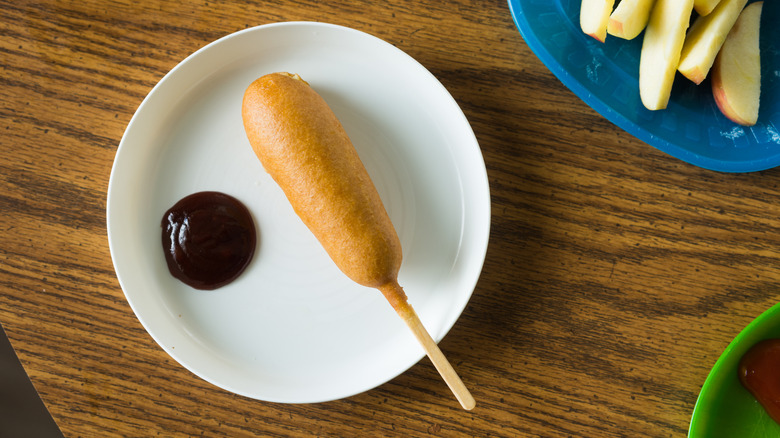 Corn dog on a white plate with sauce