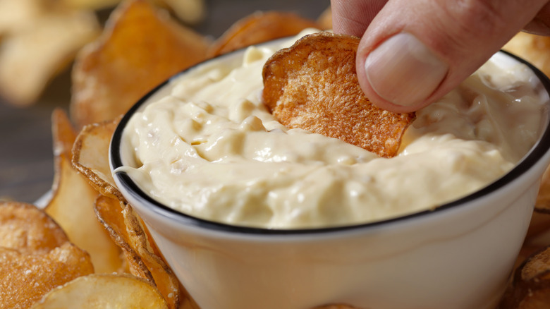 A hand dipping a chip into California onion dip