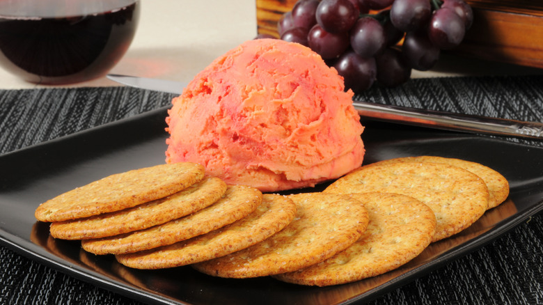 Cheese ball and crackers on a black platter with purple grapes