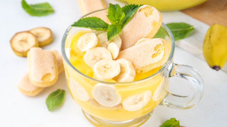Transparent mug filled with banana pudding on white table
