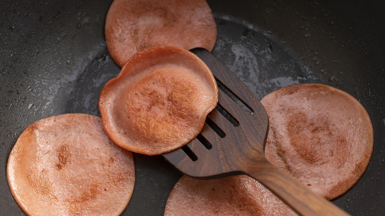 Sices of bologna being fried in a cast-iron skillet