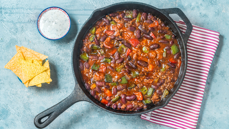 Pot of chili with side of chips on blue surface