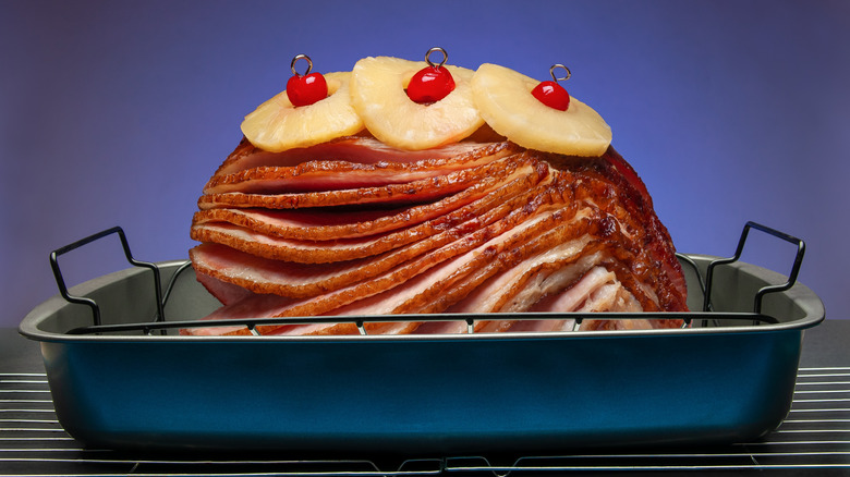 A baked ham with pineapple and cherries in a baking pan