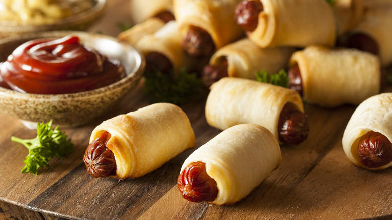Pigs in a blanket on a cutting board with ketchup