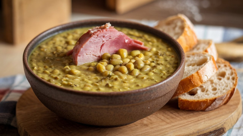 A bowl of split pea soup with ham and sliced bread