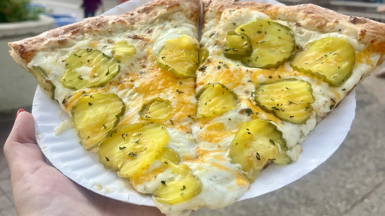 A person holding two slices of dill pickle pizza