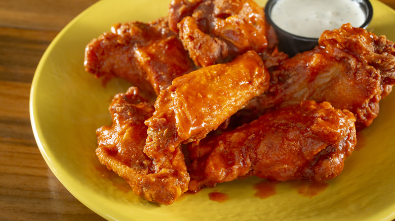 Yellow plate of buffalo chicken wings with ramekin of dipping sauce