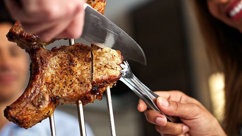 A person cutting a pork chop at Fogo de Chão