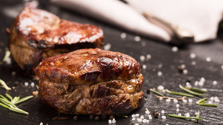 Seared filet mignon steak on black slate garnished with rosemary and salt