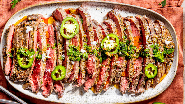 Grilled sliced flank steak on an oval white plate garnished with cilantro and jalapeño slices