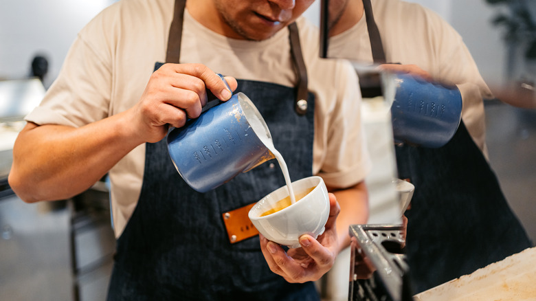 Person pouring milk into coffee cup
