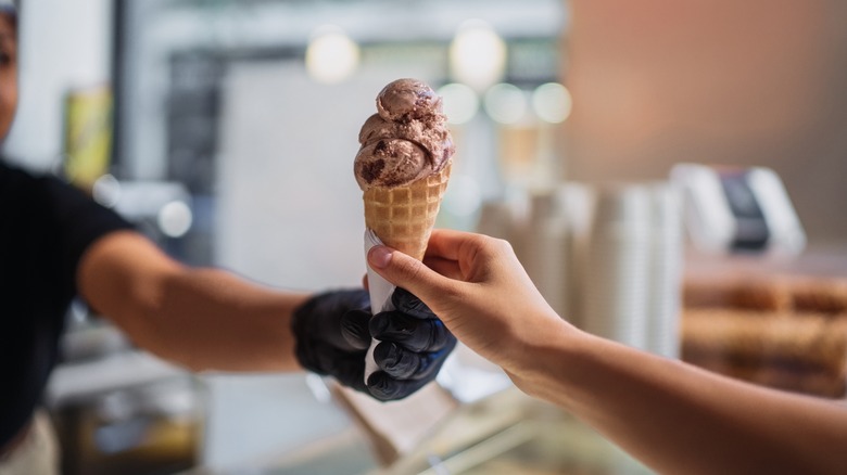 Person handing other person an ice cream cone wearing gloves