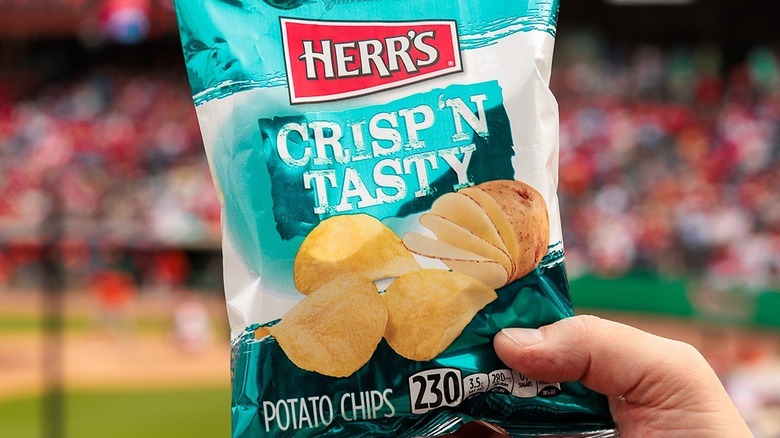 Hand holding bag of Herr's Potato Chips in a baseball stadium