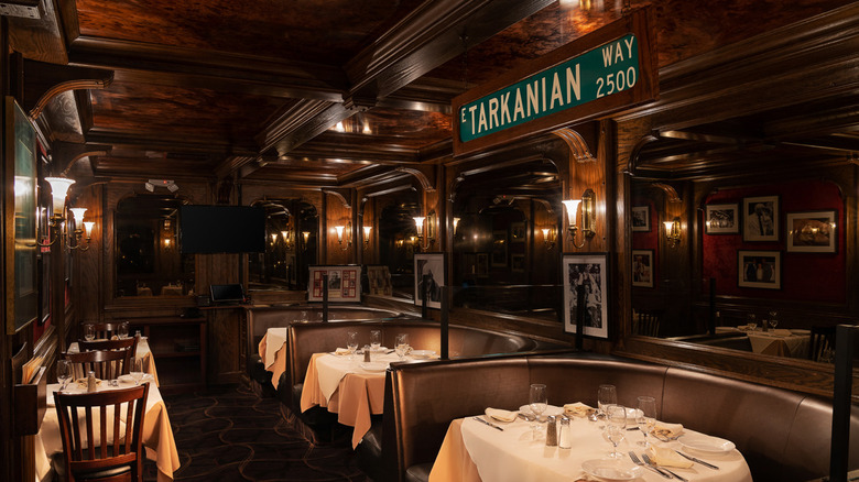 Piero's dining room with wood paneling and three rounded leather booths with white tablecloths, plus two two-tops and a street sign reading "E Tarkanian Way".