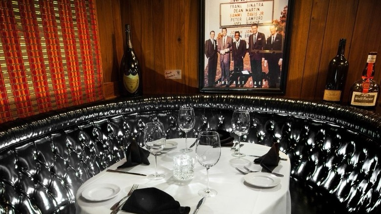 Frank Sinatra's Booth at the Golden Steer with Rat Pack photo on the wood-paneled wall, circular black banquette, white tablecloth, seating for four with wine glasses and black napkins