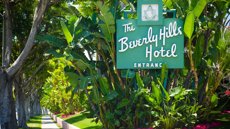 The Beverly Hills Hotel entrance sign next to sidewalk and lush greenery