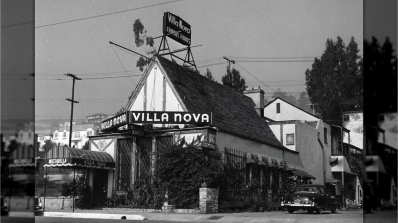 Villa Nova exterior showing small, peaked-roof, houselike building with a sign out front and on the roof