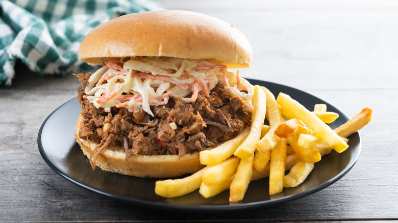 pulled pork sandwich topped with coleslaw with fries on a dark blue plate